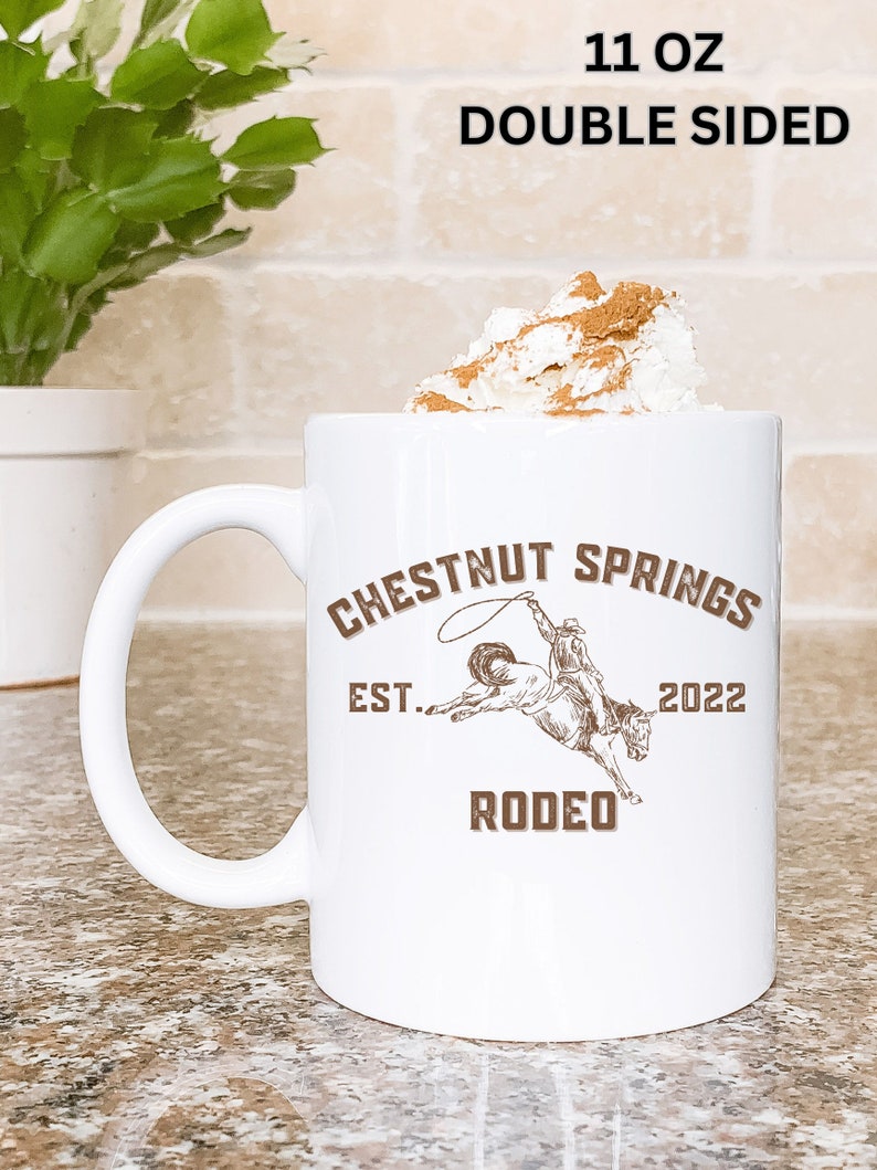 May include: White ceramic mug with a brown graphic of a cowboy riding a horse. The graphic says "Chestnut Springs Est. 2022 Rodeo". The mug is 11 ounces and double-sided.