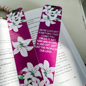 May include: Two pink bookmarks with white lilies printed on them. The text on the bookmark reads "Maybe love isn't something that comes full circle. It just ebbs and flows, in and out, just like the people in our lives."