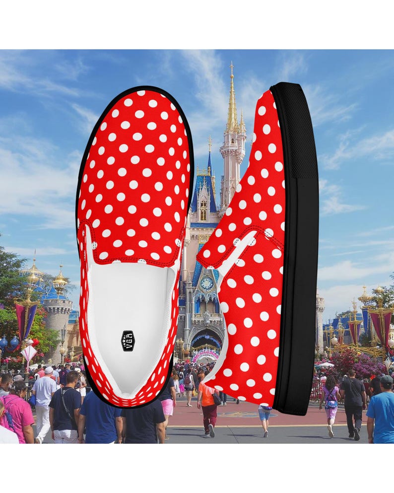 May include: Red and white polka dot slip-on shoes with black soles. The shoes are displayed against a background of a theme park with a castle and people. The shoes have a white interior and a logo.