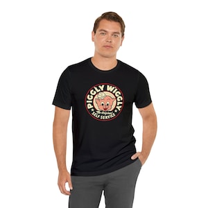 May include: Black t-shirt with a white circle graphic featuring a cartoon pig with the text "Piggly Wiggly The Original Self Service" in red and yellow.