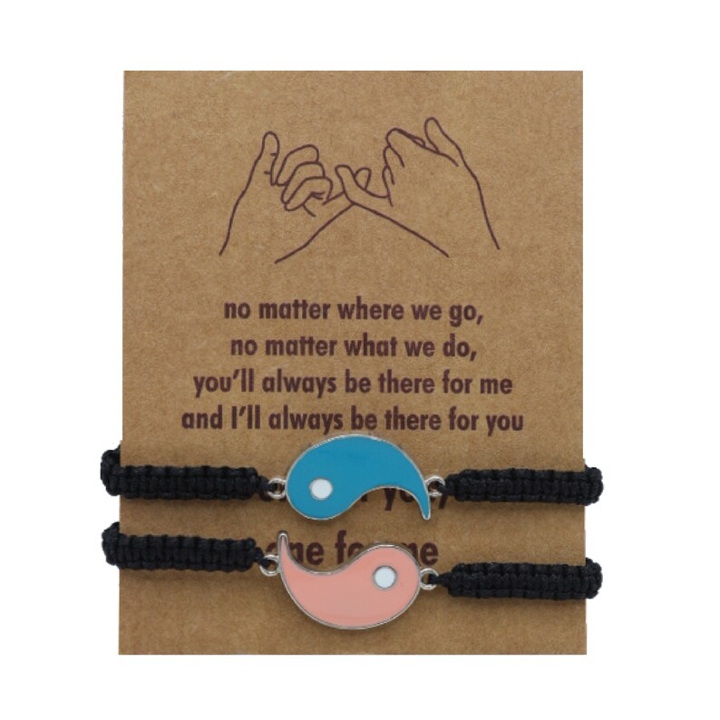 May include: Two black friendship bracelets with a yin yang charm. The charm is made of metal and has a blue and pink enamel finish. The card behind the bracelets reads: "no matter where we go, no matter what we do, you'll always be there for me and I'll always be there for you".
