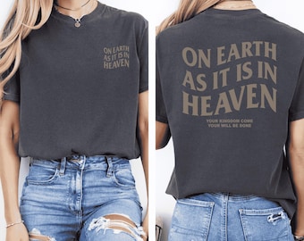 May include: A dark gray t-shirt with the text "On Earth As It Is In Heaven" printed on the front and back. The back also includes the text "Your Kingdom Come Your Will Be Done".