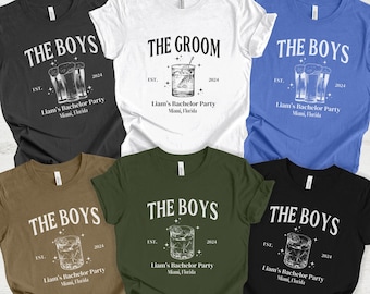 May include: A set of six t-shirts in various colors, each featuring a different design. The shirts all have the text "The Boys" and a graphic of a cocktail glass with the text "Liam's Bachelor Party" and the date "2024". One shirt has the text "The Groom" instead of "The Boys". The colors of the shirts are dark grey heather, white, heather columbia blue, heather olive, military green, and black.