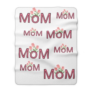 Puede incluir: Manta blanca con la palabra "MOM" en letras rosas, repetida en la superficie. Cada "MOM" va acompañado de un ramo de rosas rosas, creando un diseño floral y textual.