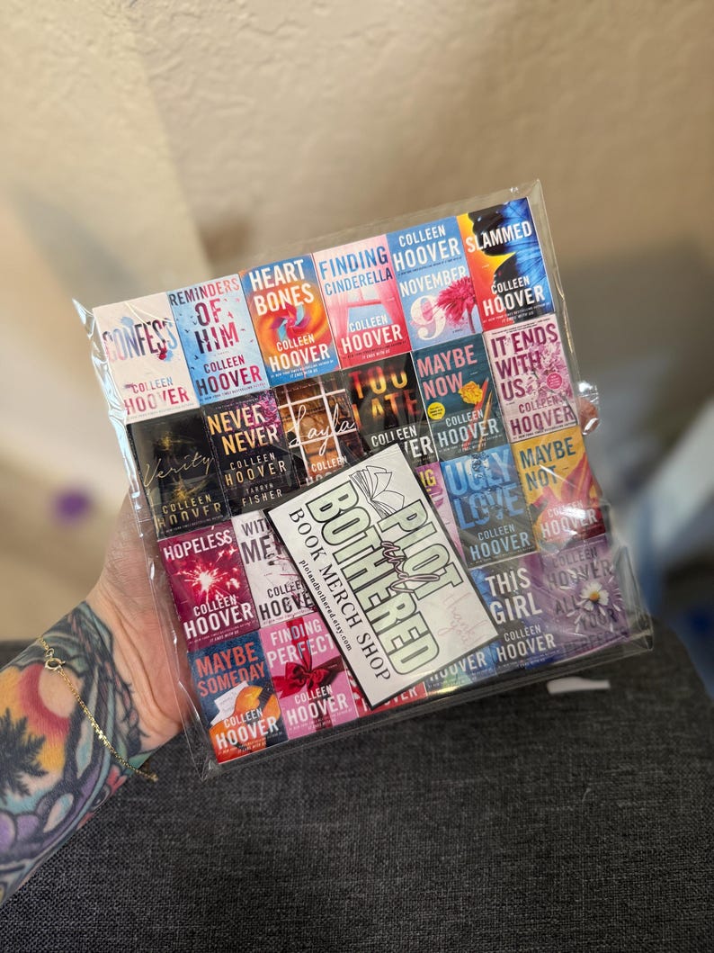 Peut inclure: Un sac en plastique transparent rempli de couvertures de livres miniatures, avec des titres tels que "Confess", "Heart Bones" et "It Ends With Us". Une carte avec "Plot Bothered Book Merch Shop" est visible. Les livres sont de Colleen Hoover.
