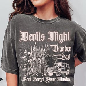 May include: A black t-shirt with a graphic print of a church, a car, and the text "Devils Night Thunder Bay Don't Forget Your Masks".