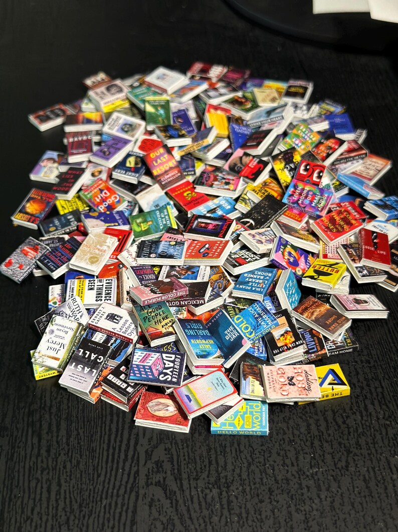 May include: A collection of miniature books with various colorful covers and titles. The books are arranged in a pile, showcasing a variety of genres and designs. Some titles visible include "Last Call", "Good Dirt", and "Hello World".