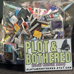 May include: A clear plastic bag filled with miniature books. The books have colorful covers and various titles. A rectangular sticker with the text "PLOT & BOTHERED Book Merch Shop" and a butterfly graphic is in front of the bag.