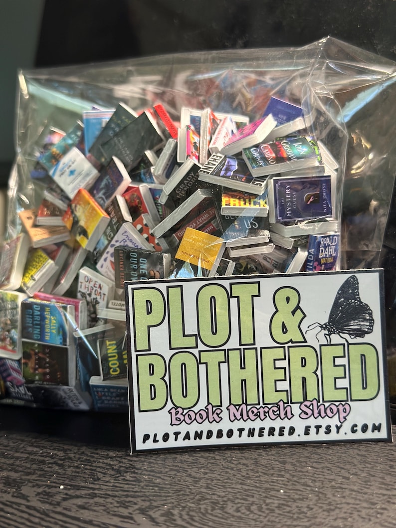 May include: A clear plastic bag filled with miniature books. The books have colorful covers and various titles. A rectangular sticker with the text "PLOT & BOTHERED Book Merch Shop" and a butterfly graphic is in front of the bag.