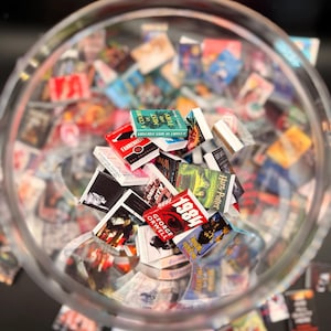 Peut inclure: Un bol en verre transparent rempli de r&eacute;pliques de livres miniatures. Les livres ont des couvertures color&eacute;es et des titres tels que "1984" de George Orwell, "Fahrenheit 451" et "A Court of Mist and Fury". Les livres sont &eacute;parpill&eacute;s dans le bol.