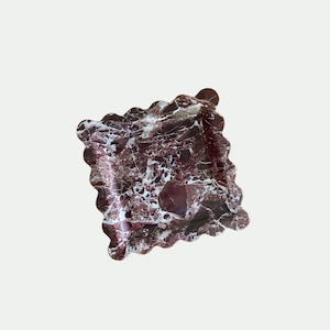 Può includere: Un vassoio in marmo rosso e bianco con un bordo a festoni. Il vassoio è realizzato in pietra naturale e ha una forma unica e organica.