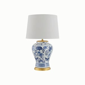 May include: A blue and white ceramic table lamp with a white lampshade. The lamp base has a gold-colored base and top, and features a detailed blue pattern. The lampshade is a simple, white cone shape.