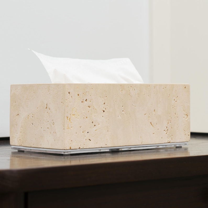 May include: A beige travertine tissue box cover with a clear acrylic base. The tissue box cover has a rough, textured surface.