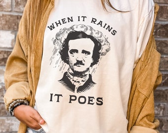 May include: A white t-shirt with a black illustration of Edgar Allan Poe with a cloud above his head and rain falling. The text "When it rains it POES" is printed on the shirt.
