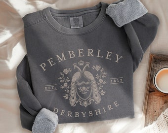 May include: A gray sweatshirt with a cream-colored design featuring the text "Pemberley Est. 1813 Derbyshire" and a crest with two peacocks.