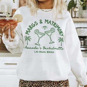 May include: White sweatshirt with green text that reads "Margs & Matrimony" with a diamond and two margarita glasses. The text "Amanda's Bachelorette Las Vegas, Nevada" is below the graphic.