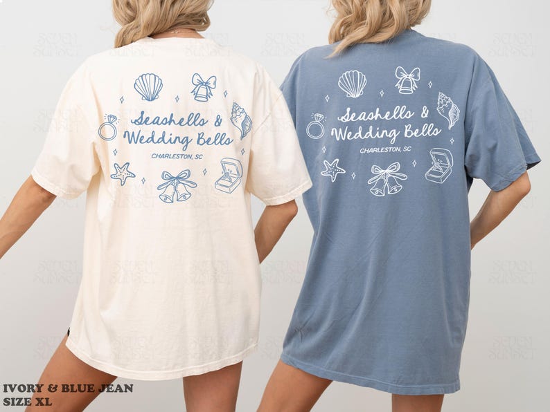 K&ouml;nnte beinhalten: Zwei &uuml;bergro&szlig;e T-Shirts, eines in Elfenbein und eines in Blau, mit dem Text "Seashells & Wedding Bells" und zugeh&ouml;rigen Grafiken. Das Design umfasst Muscheln, Glocken, einen Ring und einen Seestern. Die Shirts sind in Gr&ouml;&szlig;e XL.