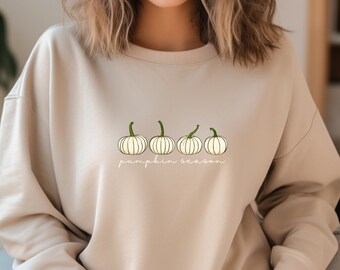 May include: A beige sweatshirt with a line of five white pumpkins and the text "pumpkin season" in a cursive font.