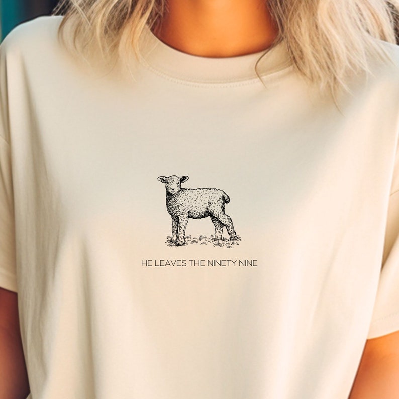 May include: A cream-colored t-shirt with a black and white illustration of a lamb. The text "HE LEAVES THE NINETY NINE" is printed below the image.