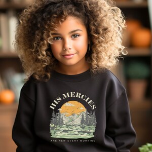 Könnte beinhalten: Schwarzer Pullover mit einem Vintage-Grafikdesign, das eine Berglandschaft und den Text "His Mercies Are New Every Morning" zeigt.