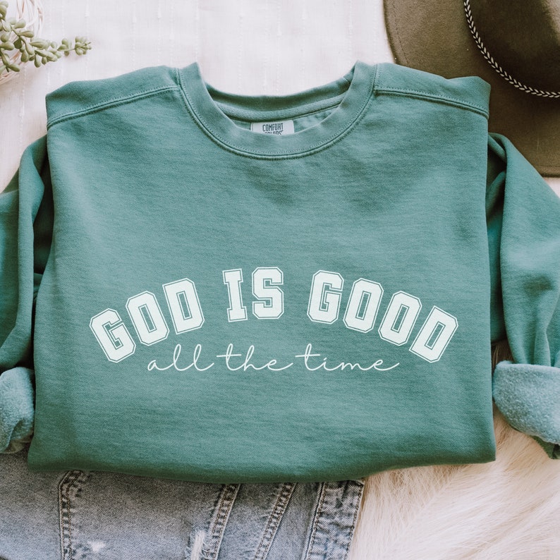 May include: A teal green sweatshirt with the text "GOD IS GOOD all the time" in white.
