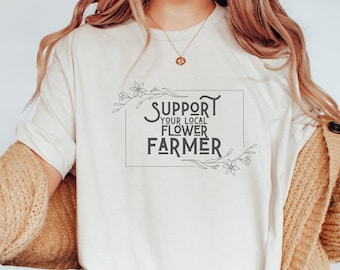Könnte beinhalten: Ein weißes T-Shirt mit einem floralen Design und dem Text "Support Your Local Flower Farmer" in einem schwarzen Rechteck.