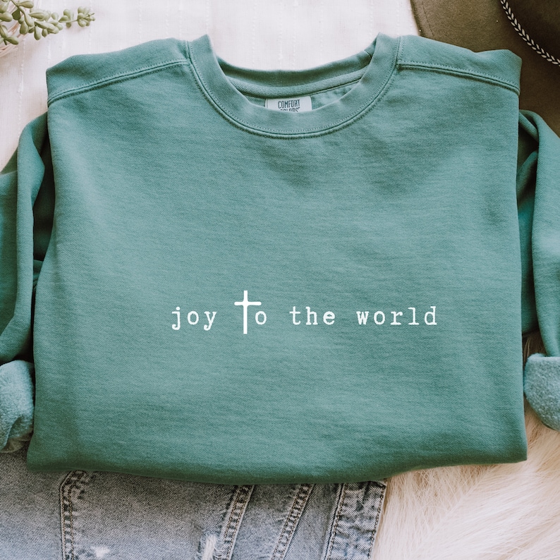 May include: A teal green sweatshirt with the text "joy to the world" and a white cross printed on the front.