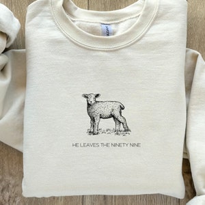 May include: A beige sweatshirt with a black and white illustration of a lamb and the text "He leaves the ninety nine".