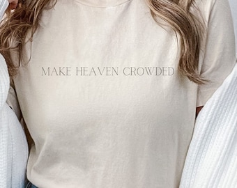 Op de afbeelding: Een beige T-shirt met de tekst "MAKE HEAVEN CROWDED" gedrukt op de voorkant.
