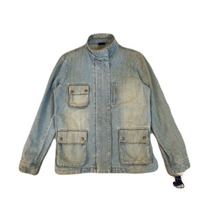May include: Light blue denim jacket with a stand-up collar and four front pockets. The jacket has long sleeves and a button-up front. The denim has a faded, worn look. A tag is attached to the sleeve.