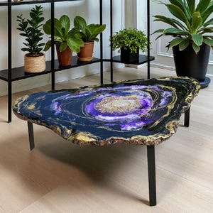 Può includere: Un tavolino da caffè artigianale con piano in resina. Il tavolo presenta un design a vortice blu scuro, nero e oro con un punto focale centrale viola e oro. Il tavolo è sostenuto da gambe in metallo nero.