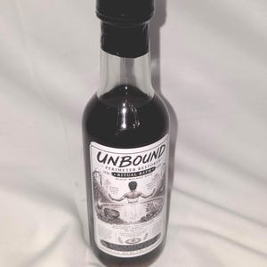 May include: A clear glass bottle filled with a dark liquid, featuring a black cap and a white label. The label displays the text UNBOUND PERIMETER RESTORED RITUAL BATH BLACK WALNUT BATH, along with an illustration of a figure and text at the bottom.