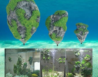 May include: Three artificial aquarium decorations shaped like floating islands. The islands are gray with green moss and have a black base. The image also shows the decorations in an aquarium with fish and plants.
