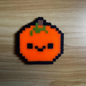 May include: A small orange pumpkin with a green stem and a black smiling face. The pumpkin is made of felt and is a cute decoration for Halloween.