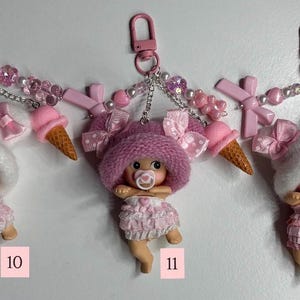 May include: Three keyrings with baby doll charms. Each doll wears a pink dress and hat, and has a dummy. The keyrings have pink clasps, decorative beads, bows, and a miniature ice cream cone. Numbers 10, 11, and 12 are visible.