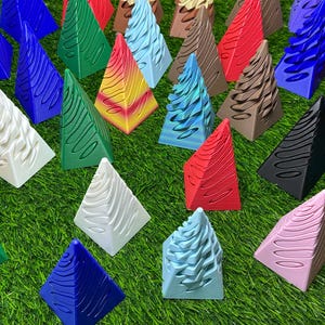 May include: A collection of colorful, patterned pyramid-shaped ornaments. The ornaments are made of a variety of materials, including wood, plastic, and metal. They are all different sizes and shapes, and they are arranged in a random pattern on a green surface.
