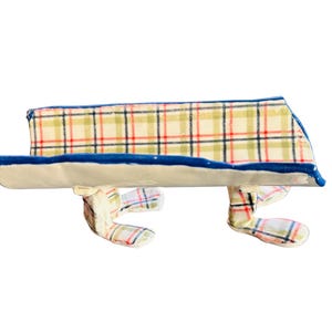 May include: A whimsical ceramic bench with a cream-colored seat and a blue trim. The back of the bench features a plaid pattern in red, green, and black. The bench has two pairs of plaid-patterned feet.