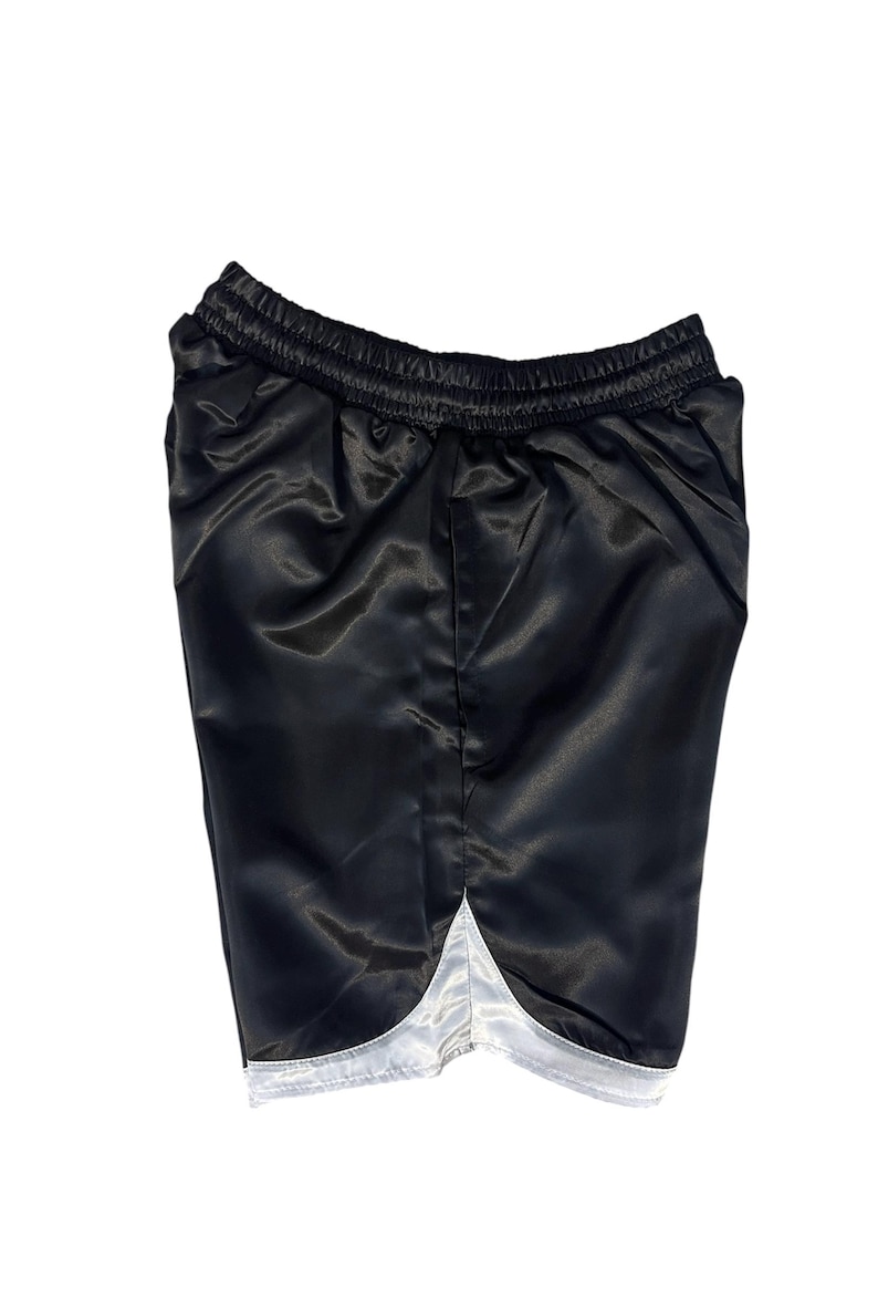 May include: Black satin shorts with a white trim along the bottom hem. The shorts have an elasticated waistband. The fabric has a shiny appearance. These athletic shorts are suitable for sports or casual wear.