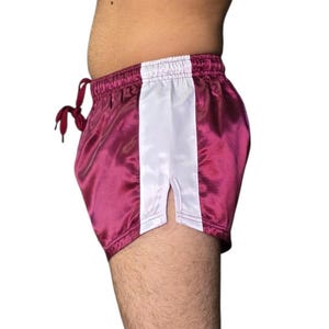Puede incluir: Pantalones cortos de sat&eacute;n color burdeos con una franja vertical blanca en el lateral. Los pantalones cortos tienen cintura con cord&oacute;n y abertura en el dobladillo. La tela es brillante, de unos 25 cm de largo.