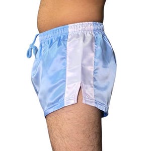 Puede incluir: Shorts de sat&eacute;n azul claro con una franja vertical blanca en el lateral. Los shorts tienen cintura con cord&oacute;n y abertura en el dobladillo. La tela tiene un ligero brillo. Estilo retro.