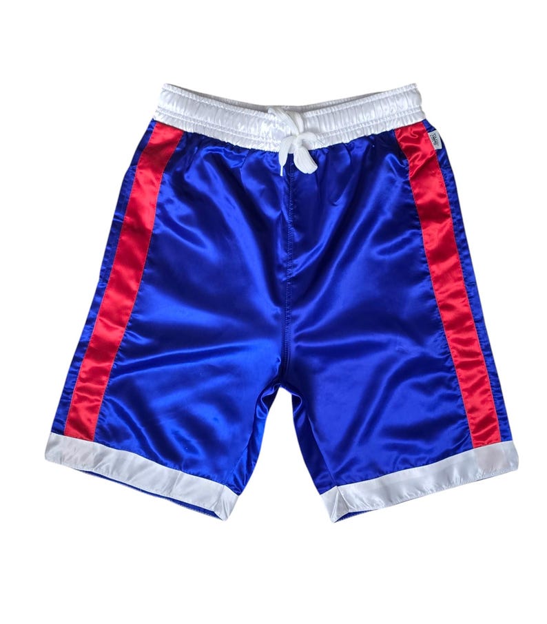 K&ouml;nnte beinhalten: Blaue Satin-Shorts mit roten und wei&szlig;en Biesen. Die Shorts haben einen wei&szlig;en Bund und einen Kordelzug.