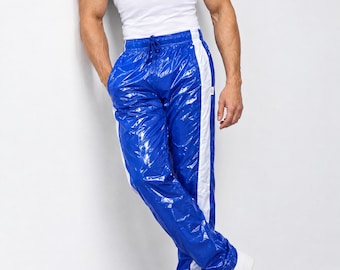 May include: A pair of glossy, royal blue track pants featuring a white vertical stripe down each leg, an elastic waistband with a drawstring, and a shiny, reflective finish. The pants are paired with a plain white tank top and white sneakers.
