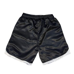 May include: Black satin shorts with white trim along the hem. The shorts have an elasticated waistband. The fabric has a shiny appearance. Suitable for athletic activities or casual wear.