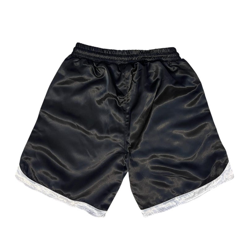 May include: Black satin shorts with white trim along the hem. The shorts have an elasticated waistband. The fabric has a shiny appearance. Suitable for athletic activities or casual wear.