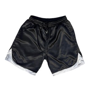 May include: Black satin shorts with a drawstring waist and white trim. The shorts have a shiny finish and a casual style. The shorts are a solid colour and are suitable for athletic activities or casual wear.