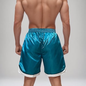May include: Teal satin athletic shorts with a white trim. The shorts have a shiny, smooth texture and a drawstring waistband. The shorts are designed for athletic activities and are a vibrant colour.