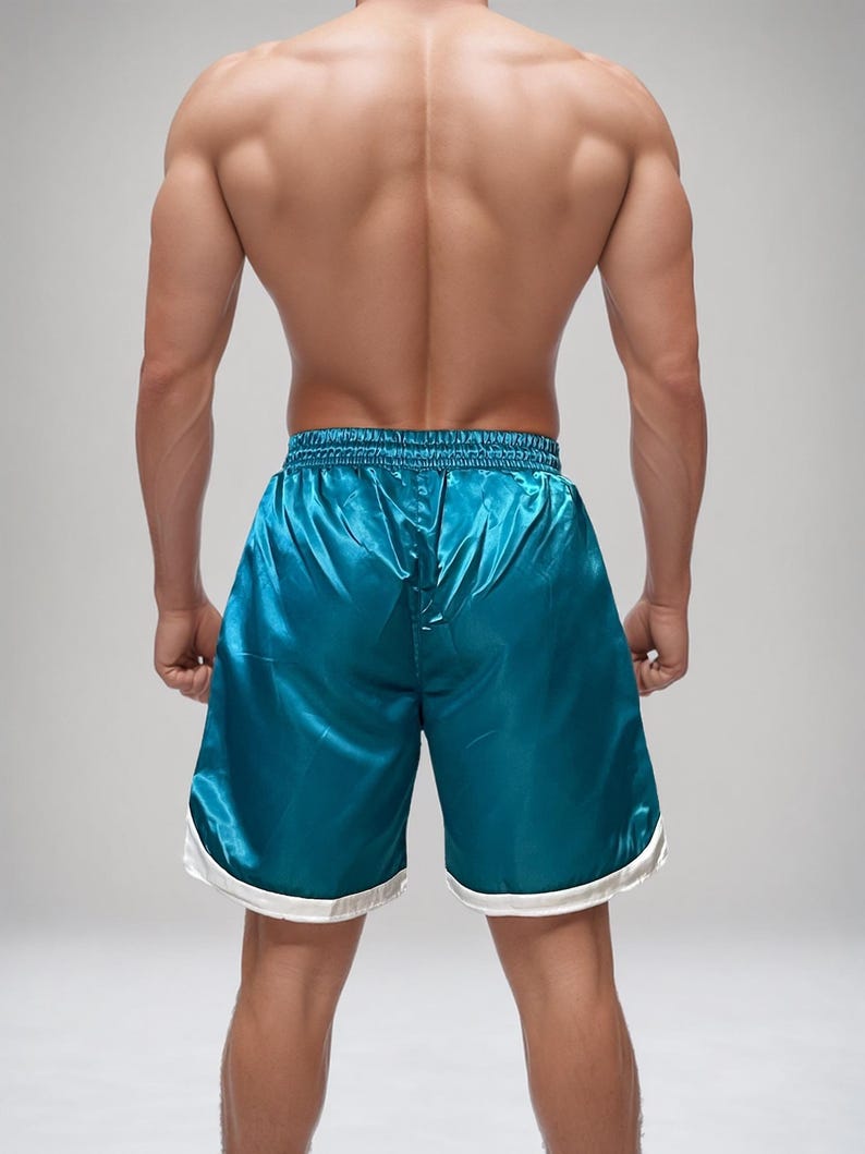 May include: Teal satin athletic shorts with a white trim. The shorts have a shiny, smooth texture and a drawstring waistband. The shorts are designed for athletic activities and are a vibrant colour.