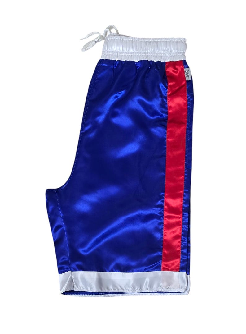 K&ouml;nnte beinhalten: Blaue Satin-Boxershorts mit einem roten Streifen an der Seite und wei&szlig;em Besatz an Taille und Saum.