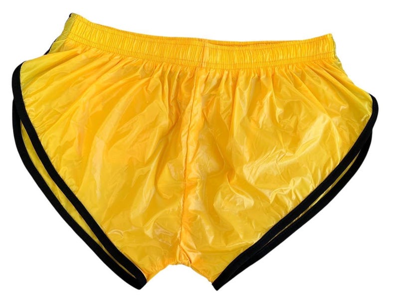 Op de afbeelding: Felgele gele sportbroek met zwarte bies. De short heeft een elastische tailleband en een glanzend, lichtgewicht materiaal. De short is ontworpen voor hardlopen of andere sportieve activiteiten.