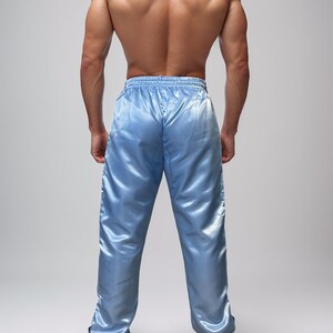 May include: Light blue satin athletic pants with a drawstring waist. The pants have a shiny, smooth texture and a relaxed fit. The pants are paired with white athletic shoes.